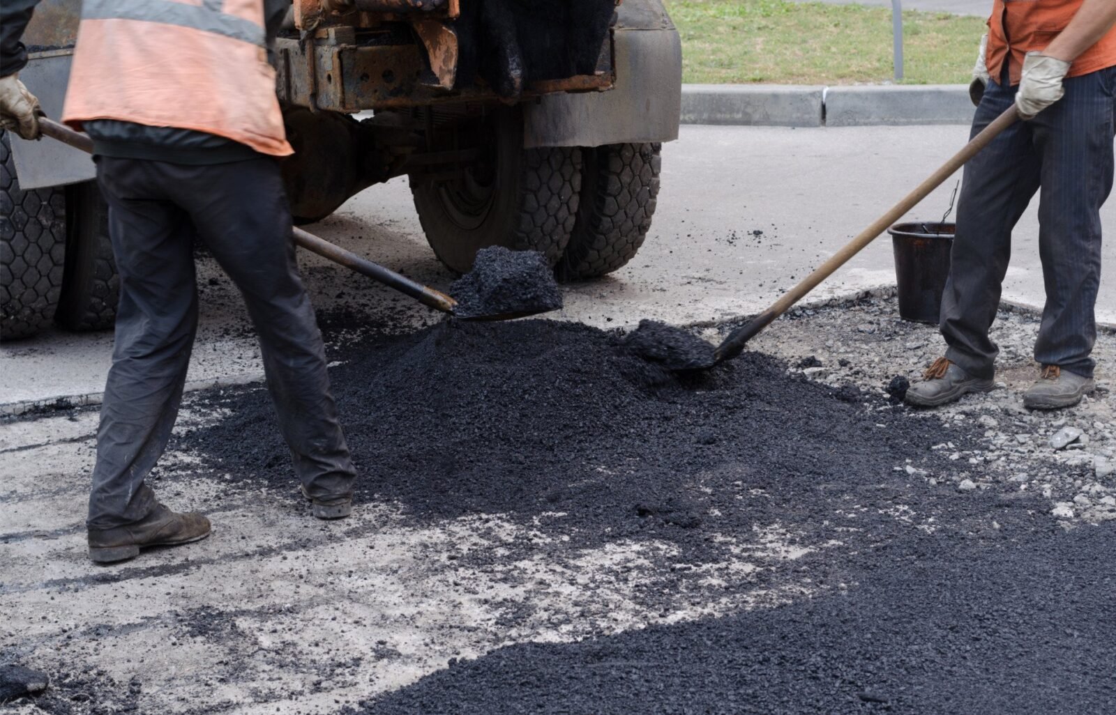 The asphalt contractors are filling in the hole with blacktop layer.